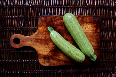 couple of zucchini  on the handmade vintage cutting board on the rattan brown tableの写真素材