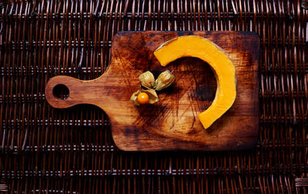 Ð¡ut into slices the pumpkin lies on vintage wooden cutting board next to the cape gooseberryの写真素材