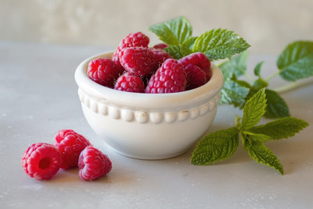 red raspberries in a white bowl with mint next to itの素材
