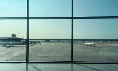 busy airport view through large glass windows, featuring parked airplanes and a clear skyの写真素材