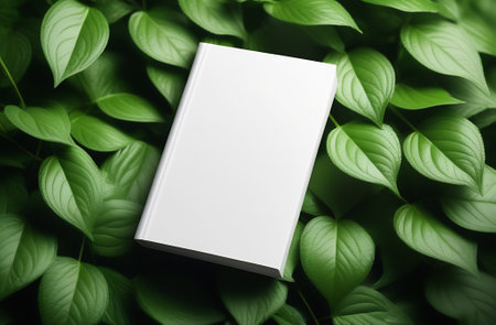 White blank book cover mockup lying on green plants.の写真素材