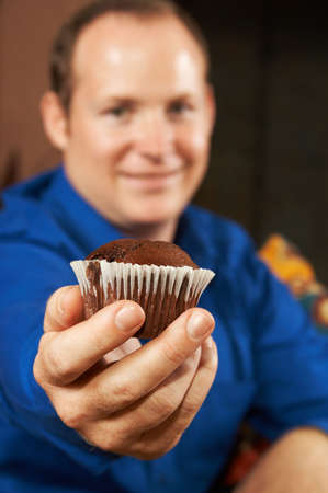 Sexy young man in blue shirt offering you a chocolate chip muffin. Shallow depth of field - muffin is in focus, man is in the background.の写真素材