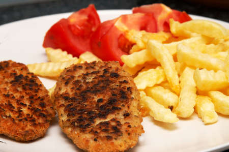 Chicken patties served with chips and sliced tomatoes on white plateの写真素材