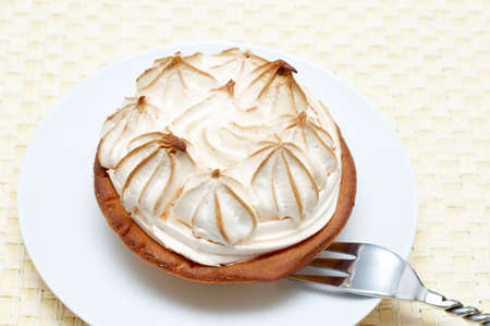 Miniature lemon meringue cake with small silver fork shot on a light wooden backgroundの写真素材