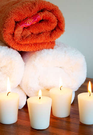 Relaxing spa scene with white and orange rolled up body towels and burning candles の写真素材