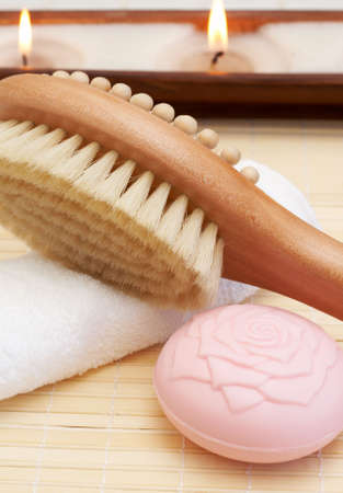 Relaxing spa scene with body brush massager, soap, white towel and candles in the background
