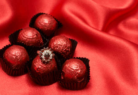 Valentines chocolate truffles with an expensive engagement ring shot on red silk backgroundの写真素材
