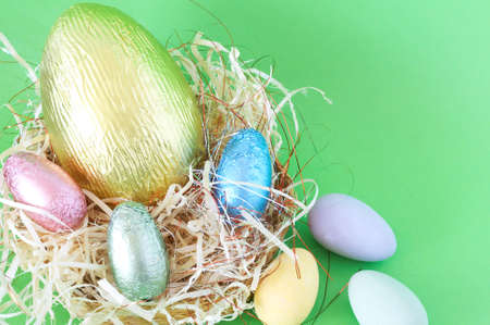 Chocolate Easter eggs in straw on green background