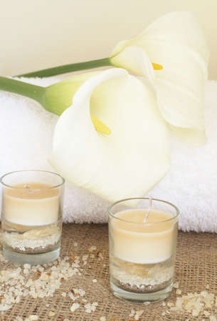 Relaxing spa scene with a white rolled up towel, white lillies, beautiful handmade candles and bath saltsの写真素材