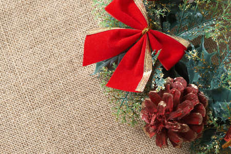 Christmas decoration with bow, leaves and cone on material background with copy spaceの写真素材