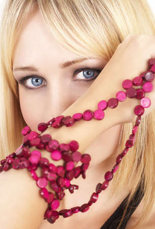 Portrait of a beautiful blonde woman with light blue eyes and dramatic make-up holding pink beads next to her face の写真素材