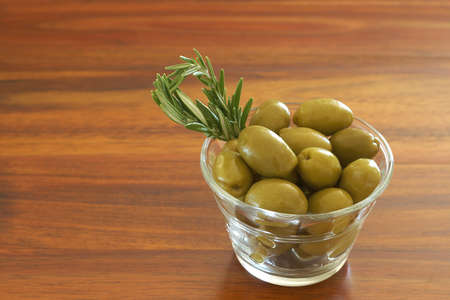 Single jar of green olives with stick of rosemary on wooden table background with copy spaceの写真素材