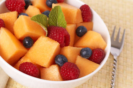 Bowl of summer fruit salad with raspberries, melon, blueberries and mint leaves in white bowlの写真素材