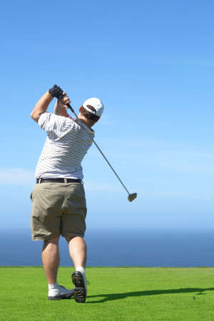 Young male golfer hitting the ball from the tee box next to the ocean on a beautiful summer day の写真素材