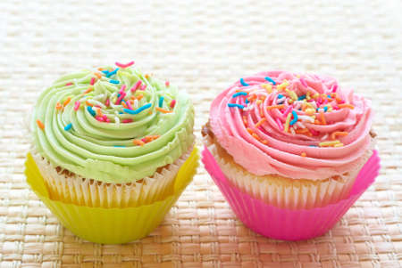 Fresh vanilla cupcakes with strawberry and lime icing on woven straw backgroundの写真素材