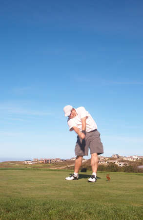 Young male golfer hitting the ball from the tee box next to the ocean on a beautiful summer day の写真素材