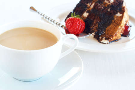 Slice of Black Forest cake with fresh cream and cherries, served on a white plate with silver fork and cup of coffeeの写真素材