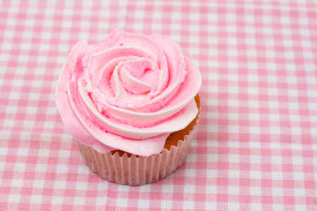 Fresh vanilla cupcake with pink rose icing on checkered backgroundの写真素材