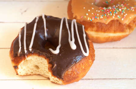 Donuts covered in caramel and chocolate icing with sprinkles on grunge wooden backgroundの写真素材