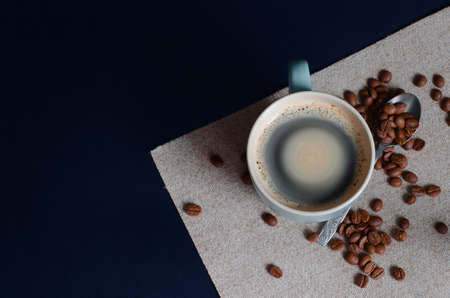 Hot coffee with foam in a cup and whole grains of coffee. A picture with a free space for text. A small vortex in the cupの写真素材