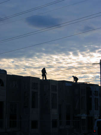 2 construction workers finishing day's work on the top of half build townhome complex, beautiful sunset in the backgroundの写真素材