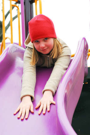 Young girl in a red hat on playground, about to go down the slidesの写真素材