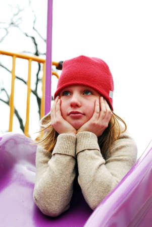 Young girl in a red hat on playground, thinkingの写真素材