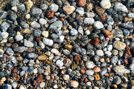 Colorful pebbles in the shallow clearest water on the beach with sun reflectionsの写真素材