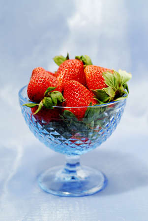Strawberries in blue glass bowl on blue backgroundの写真素材