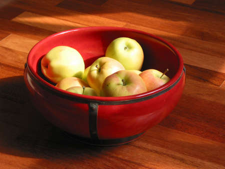 Yellow apples in a red ceramic bowlの写真素材