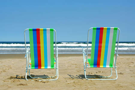Two colorful beach chairs on the ocean shoreの写真素材