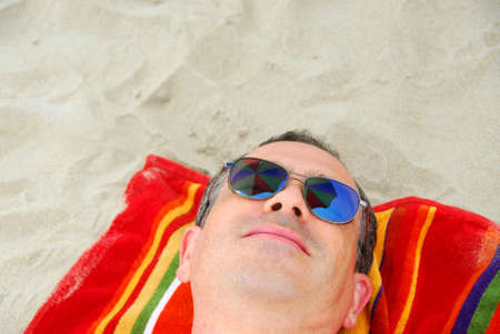 Man in sunglasses relaxing on beach, sunglasses reflect beach umbrella above.の写真素材