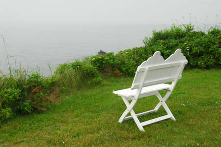 White wooden bench on the Atlantic ocean shore in Maine, US, on a foggy dayの写真素材
