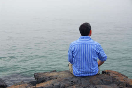 Man looking at the foggy ocean. Uncertain future concept.の写真素材
