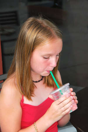 Young girl sitting in outside cafe and drinking a cool refreshing beverage