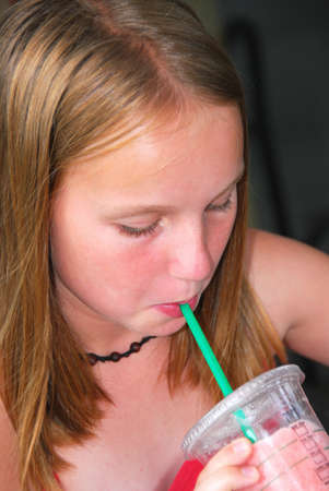 Portrait of a young girl sitting in outside cafe and drinking a cool refreshing beverageの写真素材
