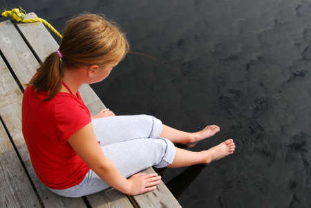 Young girl dipping feet in the lake from the edge of a wooden boat dockの写真素材