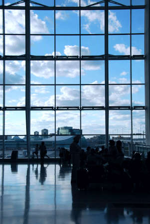 People waiting at the international airport terminal, bright blue sky outsideの写真素材