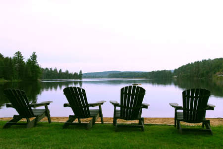Four wooden adirondack chairs on a shore of a beautiful lake at duskの写真素材
