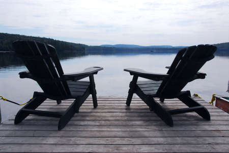 Two wooden adirondack chairs on a boat dock on a beautiful lake in the eveningの写真素材