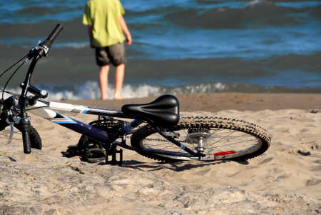 Boy walking into water with his bicycle lying on a beachの写真素材