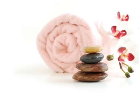 Pink rolled up towel with a stack of massage stones and orchid on white backgroundの写真素材