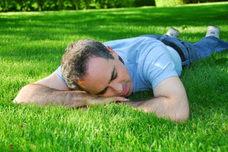 Attractive man lying on green grass in a park relaxingの写真素材