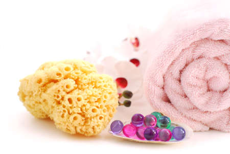 Pink rolled up towel with bath beads and natural sponge on white backgroundの写真素材