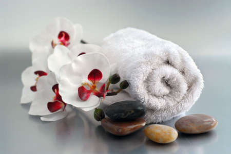 White rolled up towel with massage stones and an orchidの写真素材