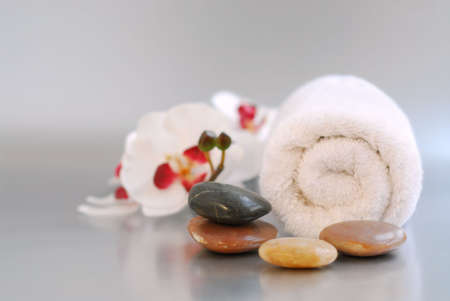 White rolled up towel with massage stones and an orchidの写真素材