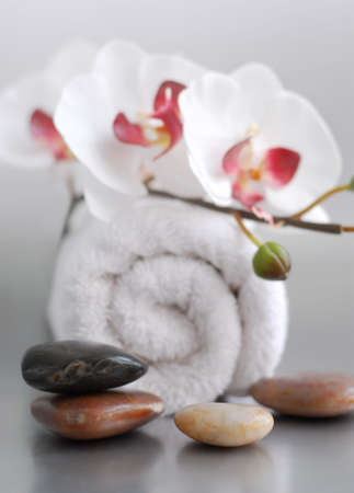 White rolled up towel with massage stones and an orchidの写真素材