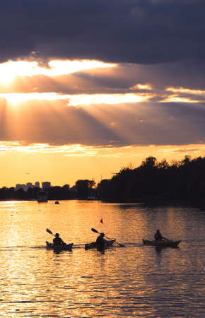 Group of people canoeing at sunset with sunrays shining through cloudsの写真素材
