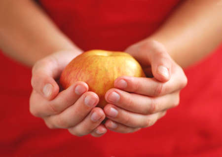 Child's hands holding an apple on red backgroundの写真素材