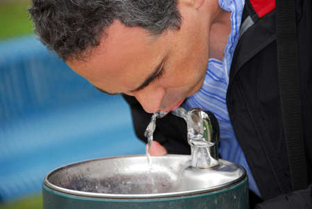 A man drinking water from a water fountain in a parkの写真素材